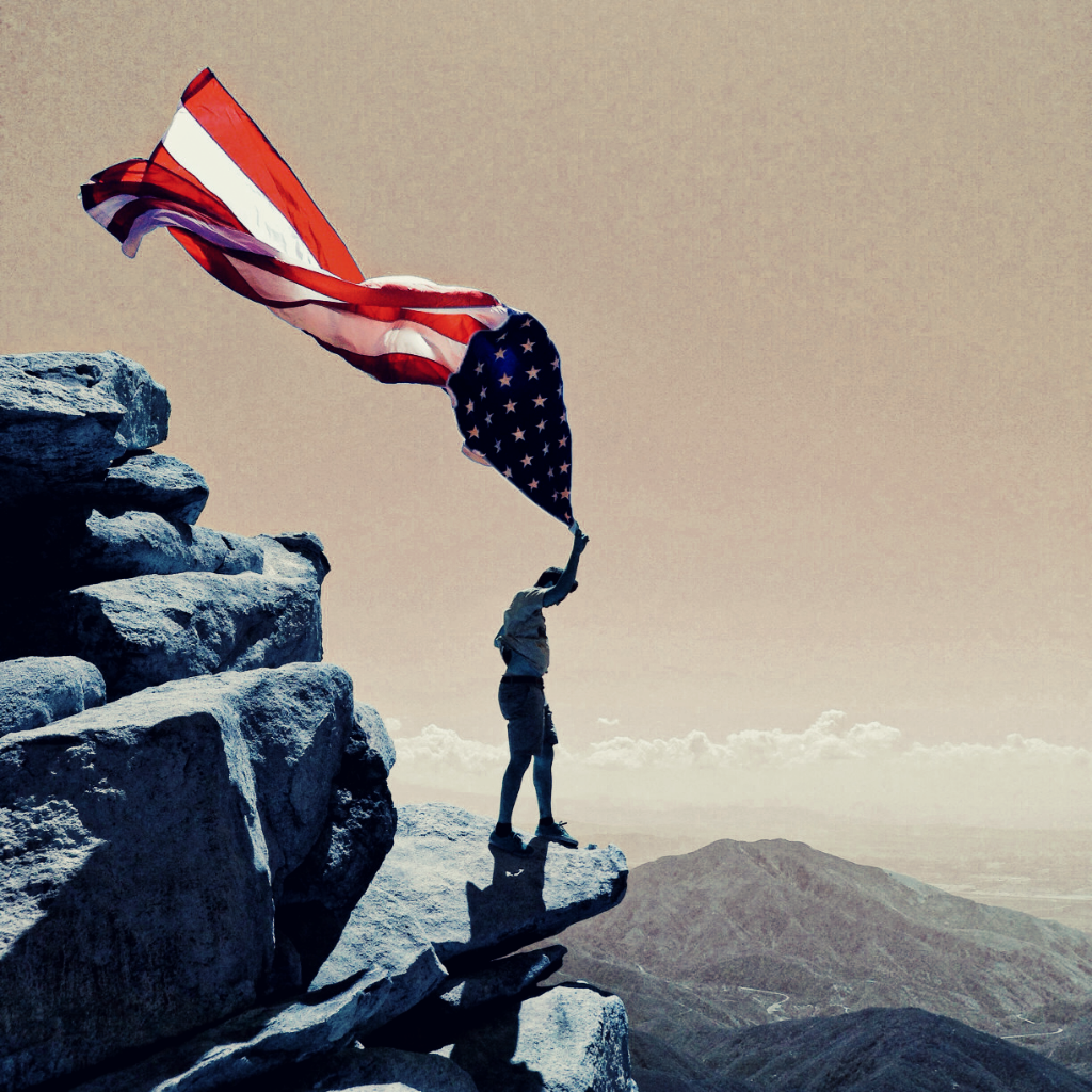 Man on a cliff holding American flag